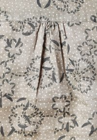 Stof med blomstermønster, hvor grå blomster og blade er trykt på en beige baggrund med prikker. Har en læg i midten for tekstur.