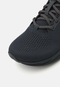 Baskets de sport gris foncé avec un dessus en mesh texturé, lacets plats et semelle rembourrée, dotées d'un bout arrondi et d'un détail de marque subtil.