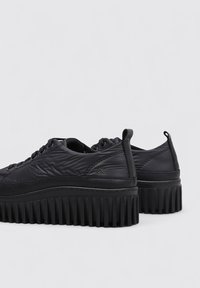 Zapatillas de plataforma negras con parte superior texturizada, punta redonda y suela estriada. Incluyen detalles cosidos y lengüetas en el talón.