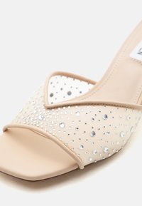 Μπεζ mule με ανοιχτά δάχτυλα και διάφανο διχτυωτό επάνω μέρος διακοσμημένο με μικρές και μεσαίες διαυγείς στρας, σε λευκό φόντο.