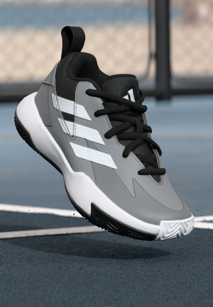 Chaussure de sport grise avec des accents noirs et trois bandes blanches. Elle présente un dessus synthétique lisse, un design à lacets et une semelle en caoutchouc.