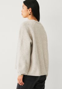 Pull en maille gris clair et duveteux avec une coupe ample, un col arrondi et des manches longues, doté de poignets et d'un ourlet côtelés.