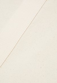 Vahvistettu puuvillakangas off-white-värissä, jossa on teksturoitu pinta. Paksu kudottu hihna kulkee kangasta vinottain, peittäen kerroksia.