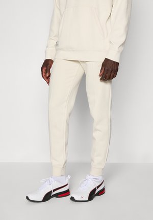 Cream-colored hooded sweatshirt with textured fabric, front pocket, and matching jogger pants. Footwear features white, black, and red accents.