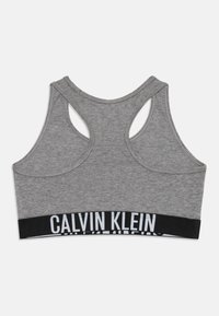 Pilkas medvilninis sportinis liemenukas su lenkta nugaros dalimi ir juodu elastingu diržu, ant kurio baltomis raidėmis yra užrašas "CALVIN KLEIN".