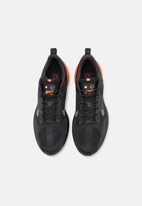 Svarta träningsskor med en texturerad ovandel, orange såldetaljer och grå Nike-logotyp. Har ett snörningssystem och vadderad krage.