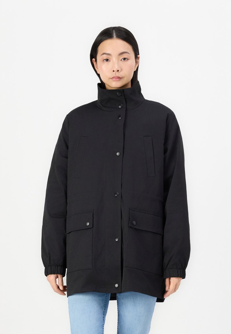 Parka noire à manches longues avec un col haut, des boutons-pression et deux poches avant ; présente des poignets élastiques et une texture lisse.