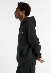 Sweat-shirt à capuche noire en tissu doux, avec une poche kangourou, logo sur la poitrine et poignets et ourlet côtelés.