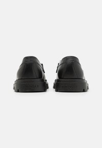 Zapatos de cuero negro con puntera redonda y suela de goma. Presenta un diseño minimalista y detalles de costura, con la marca en el tacón.