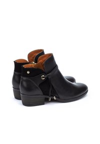 Botas de tobillo de cuero negro con un acabado suave, forro de tela marrón y detalles en hardware dorado. Presentan un tacón bajo y cordones decorativos.