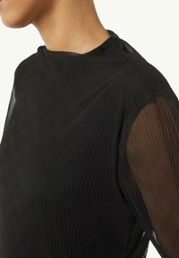 Schwarzes Top mit strukturiertem, geripptem Design und transparenten, langen Ärmeln. Der Stoff ist leicht und hat einen leichten Glanz am Ausschnitt.