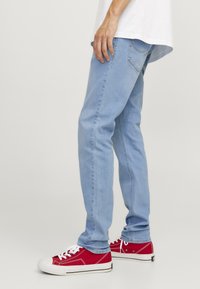 Vaqueros de mezclilla azul claro con un ajuste Slim y un ligero desgaste, combinados con zapatillas de lona rojas con cordones blancos y puntera.