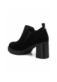 Botas de tobillo de ante negro con una gruesa plataforma y tacón cuadrado. Presentan inserciones elásticas en los lados y una lengüeta trasera para facilitar la puesta.