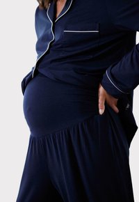 Granatowy zestaw piżam ciążowych z białym wykończeniem, składający się z koszuli zapinanej na guziki, kieszeni na piersi oraz spodni z elastycznym, marszczonym pasem.