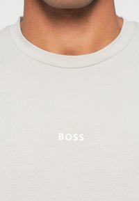 Jasnoszary t-shirt z krótkim rękawem wykonany z miękkiej bawełny, z okrągłym dekoltem i białym logo "BOSS" umieszczonym na środku klatki piersiowej.