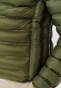 Oliwkowa kurtka puchowa z przeszyciem, z zamykaną na zamek kieszenią po lewej stronie i ściągaczami na rękawach, wykonana z gładkiego, błyszczącego materiału.
