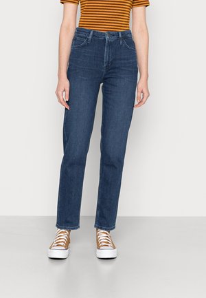 Pantalones vaqueros de cintura alta en azul oscuro con corte recto, que cuentan con bolsillos delanteros y un cierre de botón clásico. Combinados con zapatillas blancas.