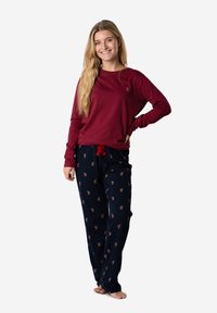 Una camiseta de manga larga color marrón combinada con pantalones de pijama azul marino con un pequeño patrón de animales. La parte superior tiene un escote redondo y un diseño ajustado.