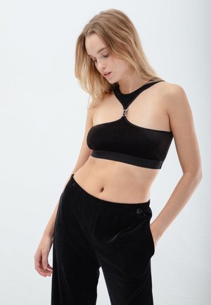 Black velvet bralette with a single strap and silver hardware detail. Paired with black velvet pants featuring an elastic waistband.