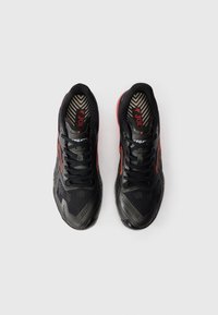 Par črnih in rdečih tekaških čevljev z vezalkami, videnih od zgoraj na beli podlagi.