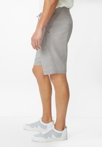 Hellgraue, gestreifte Leinen-Shorts mit elastischem Bund und Kordelzug, ausgestattet mit Seitentaschen und einem lässigen Schnitt. Kombiniert mit grauen Sneakers.