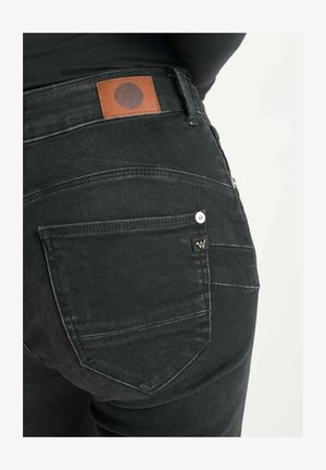 Schwarze Denim-Jeans mit einem Lederflicken, sichtbaren Nähten und einer Gesäßtasche mit einem Metalldruckknopf-Detail.