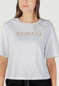 Witte cropped t-shirt van zachte stof, met gouden en strass-bewerkingen aan de voorkant die "ARMANI EXCHANGE" spellen. Korte mouwen.