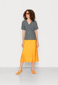 Top com padrão floral em azul-marinho e amarelo, com mangas curtas, combinado com uma saia de satin laranja fluida e saltos laranjas coordenação.
