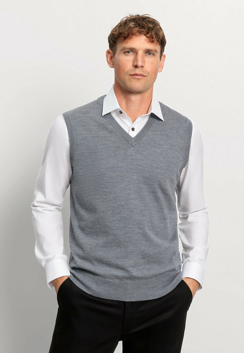 Grijze mouwloze gebreide vest met een V-hals ontwerp, gedragen over een witte hemd met kraag. Soepele textuur met geribde zoom en subtiel patroon.