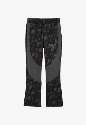 Pantalons de sport noirs avec un motif de crâne répété, des empiècements latéraux gris foncé et un design graphique violet sur le devant.