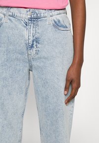 Jeans de mezclilla azul claro con un corte relajado, que incluyen cintura alta, un suave desgaste y un diseño clásico de cinco bolsillos con botón de metal.
