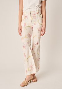 Frau trägt cremefarbene, hoch taillierte, weit geschnittene Hosen mit einem rosa-grünen Blumenmuster und beigefarbene Sandaletten mit Absatz und Riemchen.