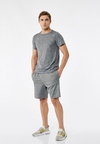 Graues sportliches T-Shirt und passende Shorts, beide aus strukturiertem Stoff. Die Shorts haben seitliche Akzentdetails und Taschen und sind mit grauen Turnschuhen kombiniert.