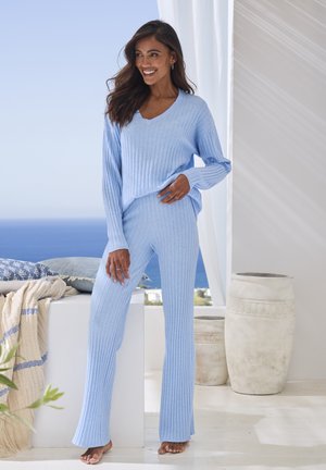 Light blue ribbed knit sweater with a v-neck and matching flared pants. The fabric appears soft and textured, set in a bright, airy environment.
