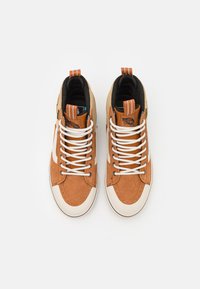 Høye sneakers med brun semsket skinn og beige tekstil på toppen. Hvit gummisåle og snøringer. Har logo-lapper på tungen og hælen.