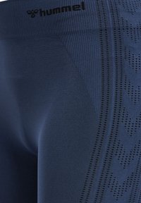 TMavě modré sportovní legíny s žebrovaným pasem a jemnými texturovanými vzory po stranách. Materiál vypadá hladce a elastiicky.