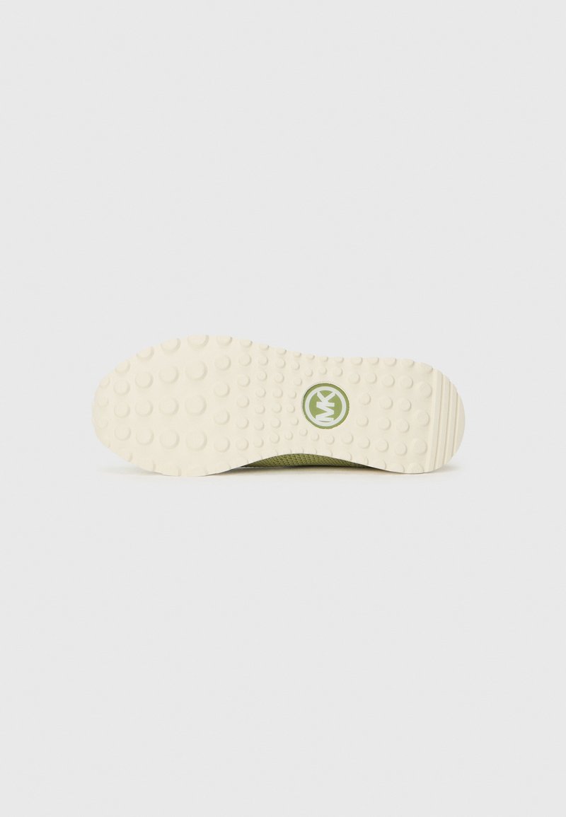 Semelle d'une sneaker verte, avec un fond en caoutchouc blanc texturé, doté de bosses arrondies et d'un logo circulaire vert.