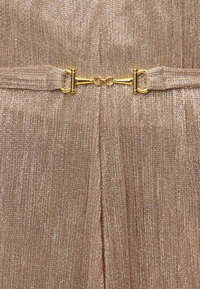 Κοντινό πλάνο υφασμάτινου μεταλλικού χρυσού με υφή και λαμπερό χρυσό κούμπωμα τύπου horsebit που συνδέει δύο υφασμάτινες λουρίδες.