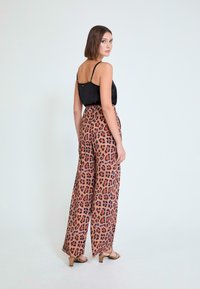 Pantalones de pernera ancha y cintura alta con diseño de estampado de leopardo, con un fondo marrón claro y manchas negras y naranjas, combinados con una blusa negra.