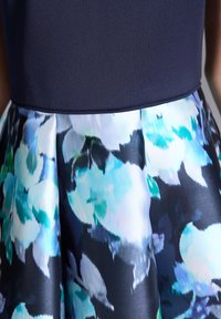 Robe avec un haut bleu marine et une jupe à motifs floraux dans des teintes de bleu et de vert, avec une texture de tissu lisse et un design plissé.