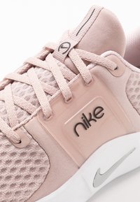 Rosa Nike träningsskor med en texturerad meshovandel, rep-snörning och en genomskinlig märkespatch med silverdetaljer på sulan.
