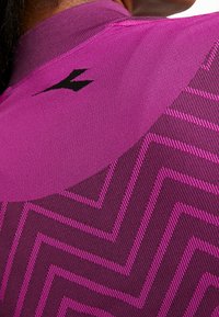 Maglietta atletica magenta con motivo a zigzag testurizzato in viola scuro. Presenta un logo nero sulla spalla e un colletto a costine.
