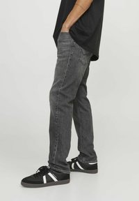 Vaqueros negros ajustados en un lavado medio, hechos de denim con una textura suave. Combinados con zapatillas negras con acentos blancos.