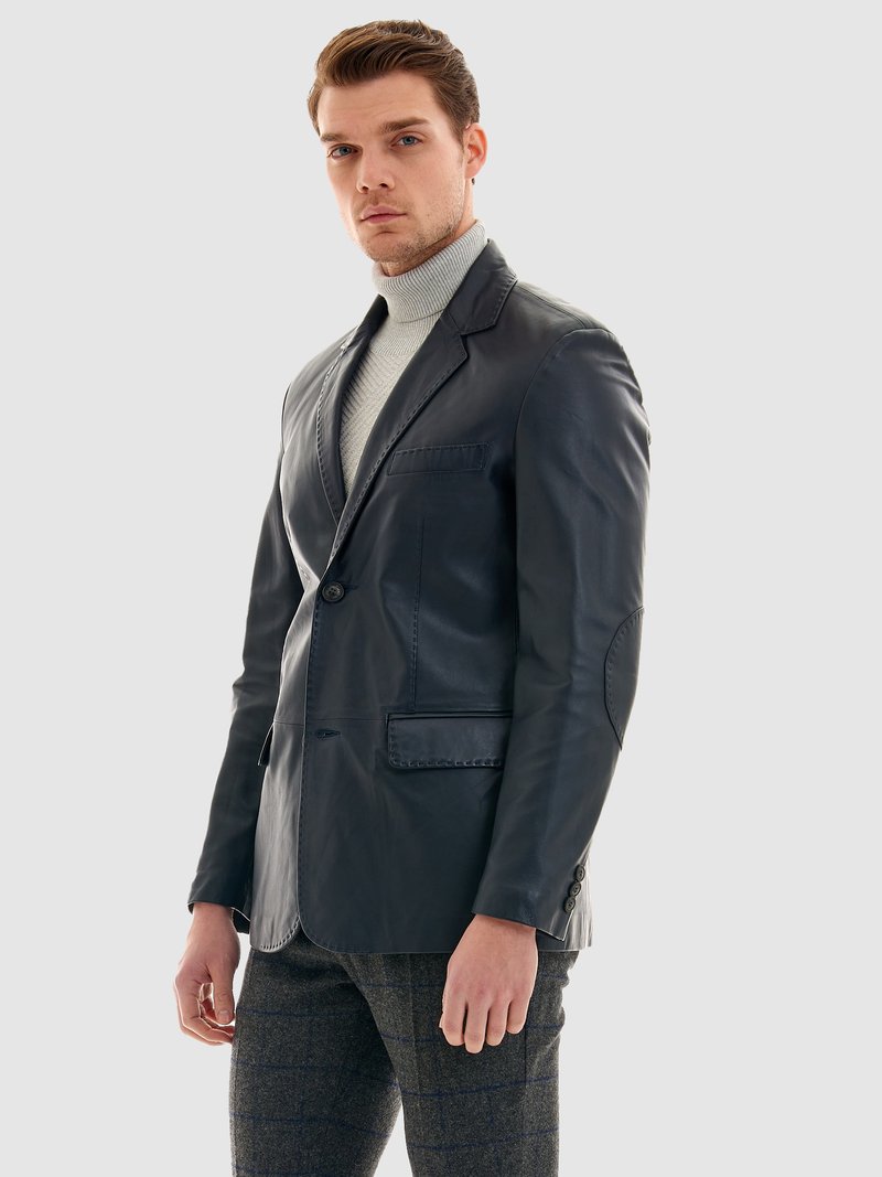 Läderblazer i mörk marinblå, med enknappslås fram, två fickor, elegant design med strukturerade axlar, ihop med en grå tröja med hög krage.