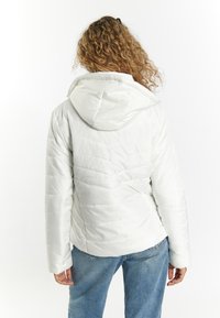 Hvid puffjakke med hætte, quiltet tekstur og en tætsiddende silhuet. Bæret over blå jeans, som fremhæver en afslappet stil.