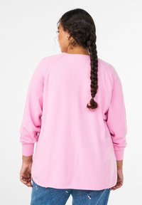 Jasnoróżowa bluza z długimi rękawami i zaokrąglonym dekoltem. Charakteryzuje się luźnym krojem i ściągaczami na mankietach. Miękka tekstura tkaniny.