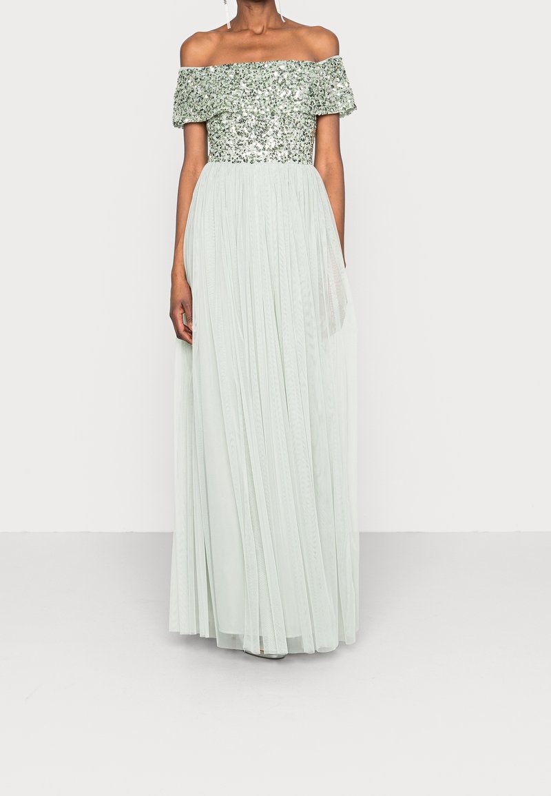 Femme portant une robe longue bustier à épaules dénudées avec un corsage argenté pailleté et une jupe plissée gris clair.