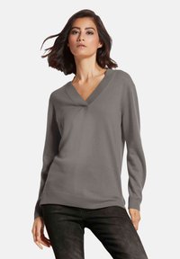 Grauer V-Ausschnitt-Pullover mit langen Ärmeln, gerippten Bündchen und Saum, glatter Textur und einem leicht lockeren Schnitt. Getragen mit dunkler Jeans.