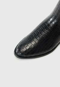 Schwarze Leder-Stiefelette mit strukturiertem Krokodil-Muster, spitzer Zehenpartie und glänzender Oberfläche. Verfügt über eine dünne, glatte Sohle.