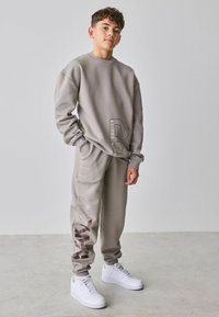 Gråt sæt af bomuld med sweatshirt og joggingbukser med et markant logodetalje, med manchetter ved anklerne og kombineret med hvide sneakers.